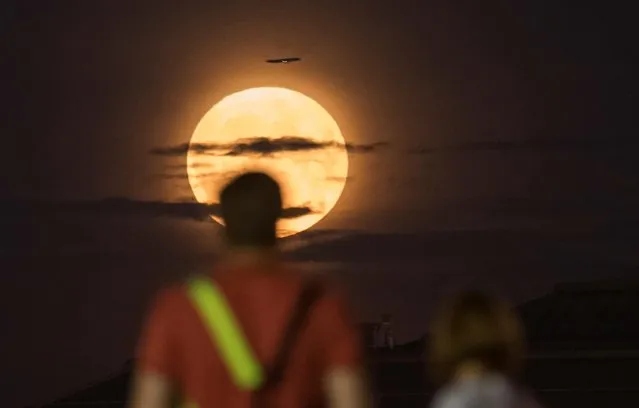 Tourists watch a full moon known as the “Buck Moon” as a commercial airplane flies by, in Moscow, Russia on July 13, 2022. (Photo by Shamil Zhumatov/Reuters)