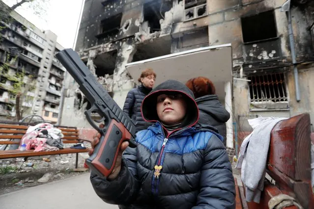Local resident Sasha, 8, holds a toy gun in front of a residential building heavily damaged during Ukraine-Russia conflict in the southern port city of Mariupol, Ukraine on April 21, 2022. (Photo by Alexander Ermochenko/Reuters)