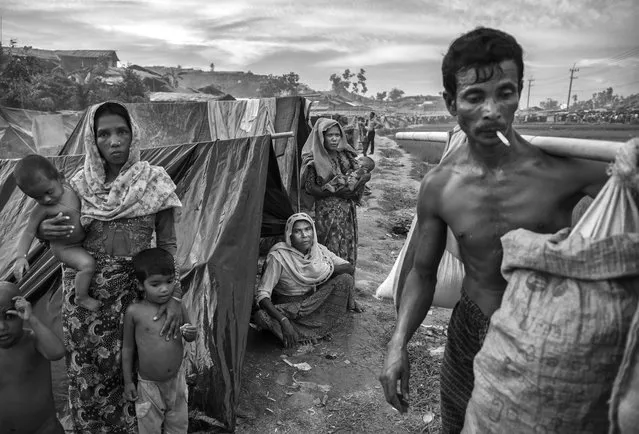 Rohingya refugees sit in front of their makeshift shelters as other arrive carrying belongings at the Palongkali Refugee Camp on September 24, 2017 in Cox's Bazar, Bangladesh. (Photo by Kevin Frayer/Getty Images)