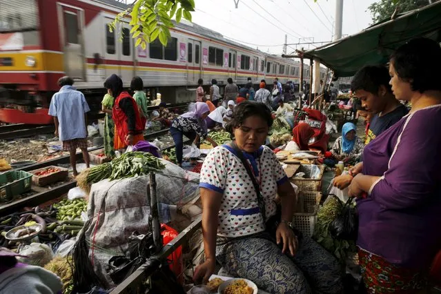 A vendor (C) serves customers at a vegetable market as a commuter train passes in Jakarta October 2, 2015. Indonesia's high annual inflation rate cooled in September and should drop more by year-end, but it likely will be 2016 before the central bank can cut interest rates to help an economy growing at its slowest pace in six years. (Photo by Reuters/Beawiharta)