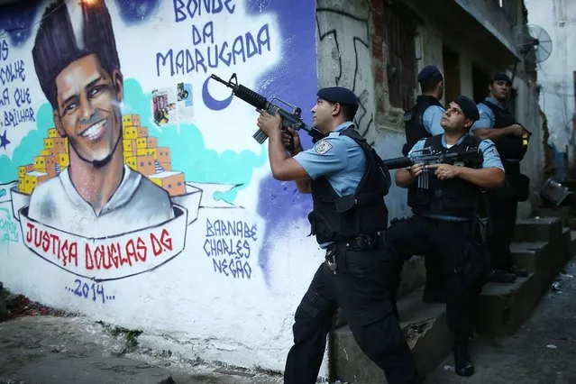 UPP (Police Pacification Unit) officers patrol next to a mural of dancer Douglas Rafael da Silva Pereira in the pacified Pavao-Pavaozinho community at the start of an investigation into the death of Pereira on May 26, 2014 in Rio de Janeiro, Brazil. (Photo by Mario Tama/Getty Images)