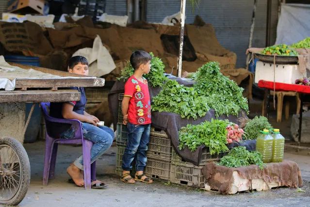 Boys stand near a vegetable stand inside a market in the rebel-held al-Shaar neighbourhood of Aleppo, Syria, September 17, 2016. (Photo by Abdalrhman Ismail/Reuters)