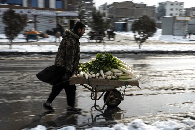 An Afghan vegetable vendor pushes his wheelbarrow along a snow laden street in Kabul on January 23, 2023. (Photo by Wakil Kohsar/AFP Photo)