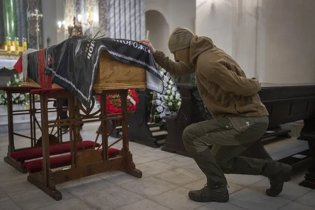 A fellow soldier mourns at the coffin of Eduard Lobau, a Belarusian volunteer soldier who was killed defending Donetsk region, in Kyiv, Ukraine, Saturday, February 4, 2023. Eduard Lobau, a Belarusian who had been fighting for Ukraine since 2015, died from a shrapnel wound while hunting tanks with a Javelin. He is now at least the 15th Belarusian to have fallen fighting for Ukraine in the last year. (Photo by Efrem Lukatsky/AP Photo)