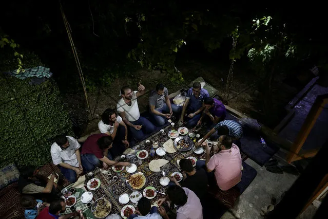 Crew of a film directed by Humam Husari (raising his hand) gather on a table after the end of filming in the rebel-held besieged town of Zamalka, in the rebel held Douma neighbourhood of Damascus, Syria October 6, 2016. (Photo by Bassam Khabieh/Reuters)