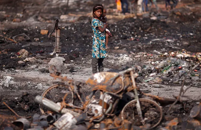 A girl carries her brother as she stands near her burnt home after a fire broke out in a slum area in New Delhi, India, April 24, 2018. (Photo by Adnan Abidi/Reuters)