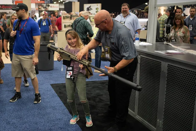 A girl attempts to balance a semi automatic .50 caliber rifle made by Barrett Firearms Manufacturing in an exhibit hall at the NRA' s annual convention on Saturday, May 5, 2018 in Dallas, Texas. (Photo by Adrees Latif/Reuters)