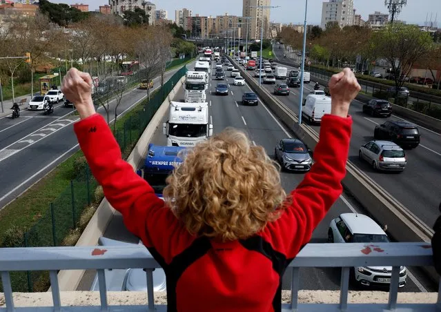 A woman shows her support for truck drivers who protest against the rise of fuel prices and against their working conditions with a slow march along the B-20 road, in Barcelona, Spain, March 21, 2022. (Photo by Albert Gea/Reuters)