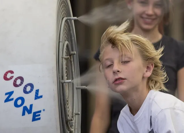 Ten-year-old Easton Martin, of Mesa, Ariz., stops to cool off in a misting fan while walking along The Strip with his family, Friday, June 28, 2013 in Las Vegas. A blazing heat wave expected to send the mercury soaring to nearly 120 degrees in Phoenix and Las Vegas settled over the West on Friday, threatening to ground airliners and raising fears that people and pets will get burned on the scalding pavement. (Photo by Julie Jacobson/AP Photo)