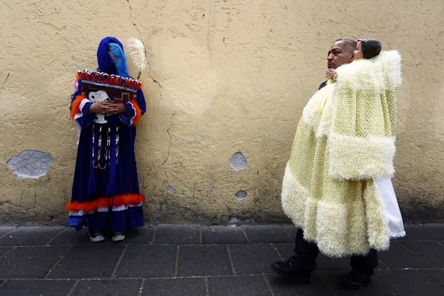 A traditional Chinelo (L) costumed dancer looks on as a man walks by with a dressed-up doll representing the baby Jesus during a celebration 40 days after the birth of Jesus, in Xochimilco on the outskirts of Mexico City, February 2, 2015. (Photo by Edgard Garrido/Reuters)