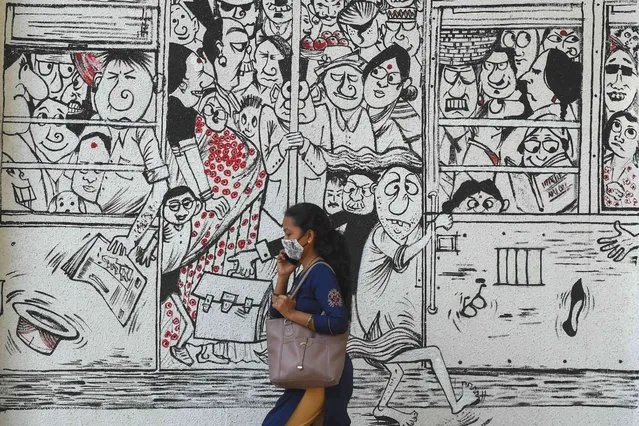 A woman walks past a mural depicting people travelling on a overcrowded public transport to raise awareness about maintaining social distancing and the use of masks, in Mumbai on March 2, 2021. (Photo by Punit Paranjpe/AFP Photo)