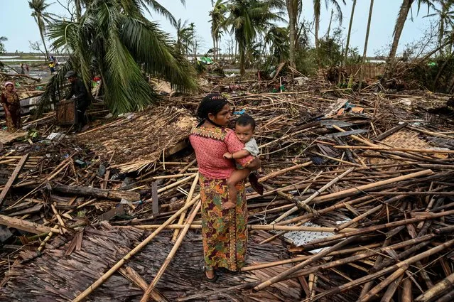 A Rohingya woman carries her baby next to her destroyed house at Basara refugee camp in Sittwe on May 16, 2023, after cyclone Mocha made a landfall. (Photo by Sai Aung Main/AFP Photo)