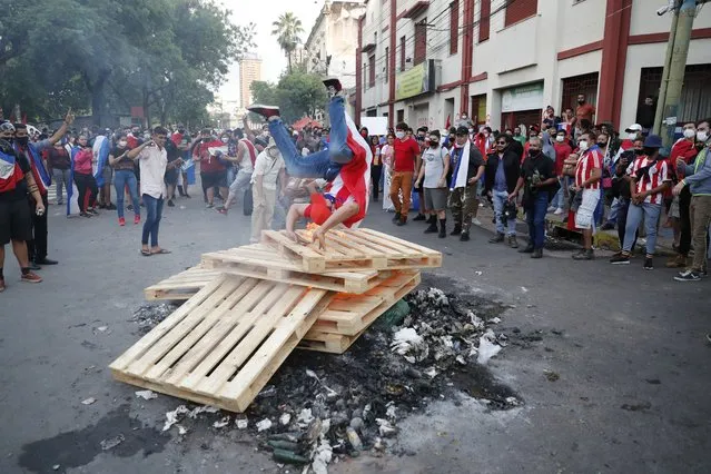 A demonstrator does a summersault over burning wood pallets placed on a street during clashes, after a failed impeachment of President Mario Abdo Benitez, in Asuncion, Paraguay, Wednesday, March 17, 2021. (Photo by Jorge Saenz/AP Photo)