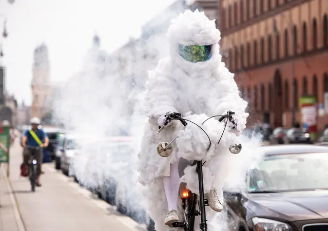 Artist Martin Nothhelfer rides as the Cloud Cyclist (Wolken Radler) on his smoke blowing bicyle at the Geschwister-Scholl-Platz in Munich, Bavaria, Germany, 28 July 2018. Nothhelfer wants to show with his performance where there is good and bad air in Munich. In addition, his bicycle blows out soap bubbles when the air is clean, but in bad air it smokes. (Photo by Lukas Barth-Tuttas/EPA/EFE)