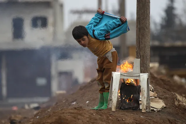 A boy warms himself around a fire in the northern Syrian rebel-held town of al-Rai, Syria on January 5, 2017. (Photo by Khalil Ashawi/Reuters)
