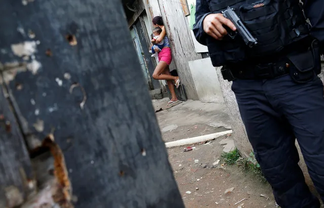 A policeman is pictured near a woman with a baby during an operation against drug dealers in Cidade de Deus or City of God slum in Rio de Janeiro, Brazil, November 23, 2016. (Photo by Ricardo Moraes/Reuters)