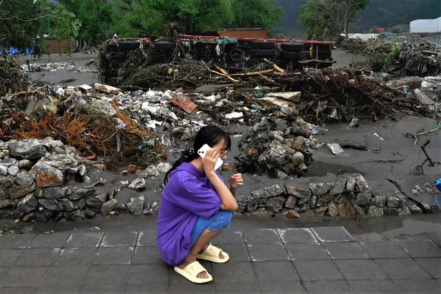 A girl speaks on a mobile phone in front of an overturned truck following heavy rains in Fangshan district in Beijing on August 1, 2023. At least 11 people were killed and 13 were missing after heavy rains lashed Beijing, state media said on August 1, in downpours that have submerged roads and deluged neighbourhoods with mud. (Photo by Pedro Pardo/AFP Photo)