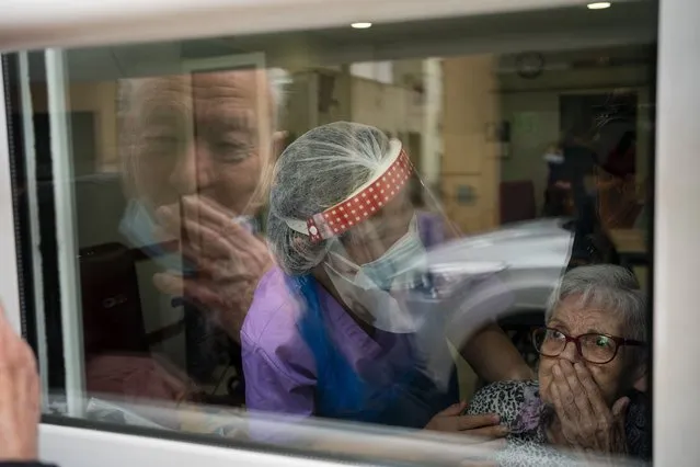 Javier Anto, 90, and his wife Carmen Panzano, 92, blow one another kisses through the window separating the nursing home from the street in Barcelona, Spain, Wednesday, April 21, 2021. Since the pandemic struck, a glass pane has separated – and united – Javier and Carmen for the first prolonged period of their six-decade marriage. Anto has made coming to the street-level window that looks into the nursing home where his wife, since it was closed to visits when COVID-19 struck Spain last spring. (Photo by Emilio Morenatti/AP Photo)