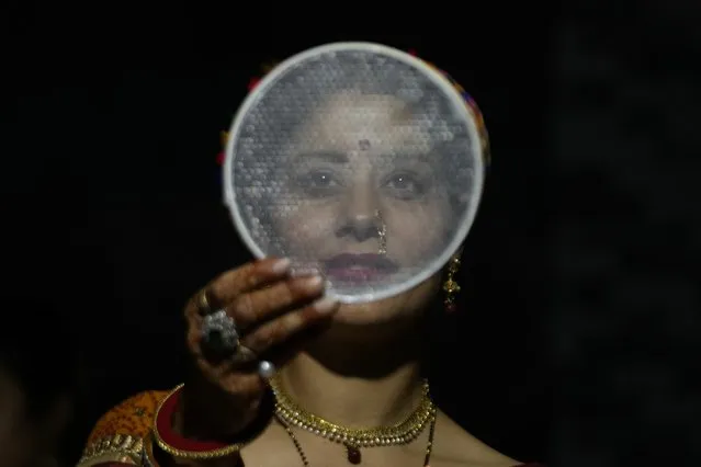 An Indian Hindu married woman looks at the moon through a sieve as part of a ritual before breaking her fast during Karva Chauth festival in Jammu, India, Wednesday, November 1, 2023. Hindu married women observe a day long fast to pray for the longevity and well being of their husbands during this festival. (Photo by Channi Anand/AP Photo)