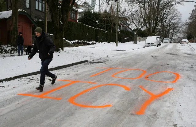 A man tests his footing on an icy hill street marked with day-glo orange spray paint, during a spell of cold weather in Vancouver, British Columbia, Canada January 6, 2017. (Photo by Chris Helgren/Reuters)