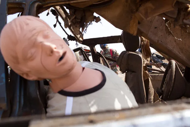In this photo taken on Thursday, February 18, 2016,  a mannequin is seen inside a vehicles that was exploded during U.S.-led Flintlock military exercises as students, rear take photos and make notes in Thies, Senegal. (Photo by Vincent Tremeau/AP Photo)