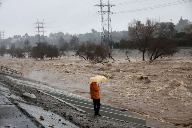 A person holding an umbrella watches the Los Angeles river during heavy rains in Los Angeles, California, U.S., February 5, 2024. (Photo by Aude Guerrucci/Reuters)