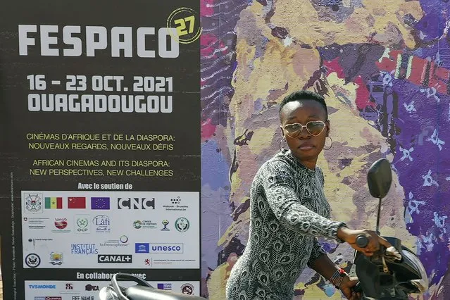 A woman pushes her scooter past the entrance of FESPACO (Pan-African Film & TV Festival of Ouagadougou) in Ouagadougou, Burkina Faso, Friday October 15, 2021. The event, now in its 52nd year, is attracting filmmakers and moviegoers from across the continent and the globe. (Photo by Sam Mednick/AP Photo)