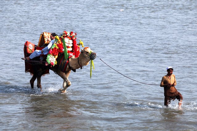 A man leads a camel with men taking a ride on it during the second day of Eid al-Fitr celebrations, along the Kabul river, as seen from Sardaryab in the outskirts of Peshawar, Pakistan on April 11, 2024. (Photo by Fayaz Aziz/Reuters)