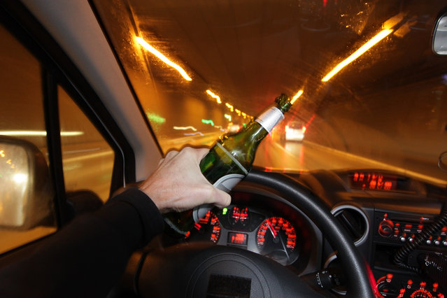 A man driving a car with a bottle of beer in his hand. (Photo by Rex Features/Shutterstock)