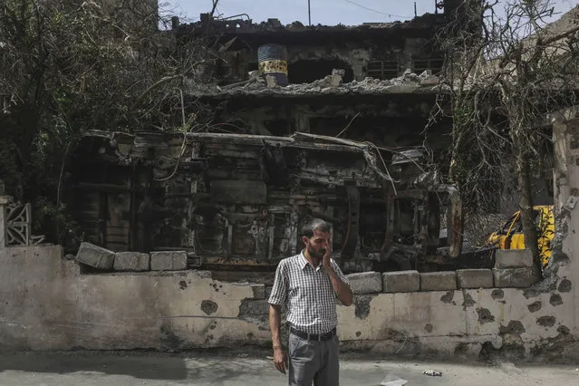 A man stands in front of a destroyed car and house in western Mosul, Thursday, May 11, 2017.  U.S.-backed Iraqi forces were moving to surround Mosul's Old City on Thursday, a week after launching a fresh push to drive Islamic State militants from areas they still hold. (Photo by Bram Janssen/AP Photo)