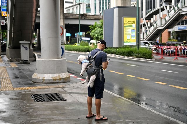 A man carries a dog on his back as he stands along a street in Bangkok on September 18, 2024. (Photo by Manan Vatsyayana/AFP Photo)