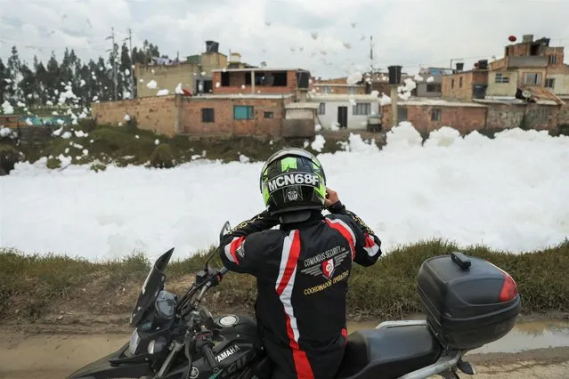 A motorcyclist takes photos with his cell phone of the polluting foam generated by a river full of waste as it is blown by the wind next to houses, in Mosquera, Colombia on April 27, 2022. (Photo by Luisa Gonzalez/Reuters)