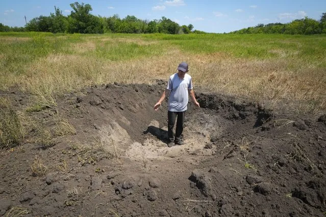 Farmer Serhiy, a local grain producer, shows a crater left by a Russian shell on his field in the village of Ptyche in eastern Donetsk region, Ukraine, Sunday, June 12, 2022. Serhiy claims he cannot sell his grains because nobody wants to come to the area which has been under Russian shelling. Ukraine is one of the world’s largest exporters of wheat and corn but Russia's invasion and a blockade of its ports have halted much of that flow. (Photo by Efrem Lukatsky/AP Photo)