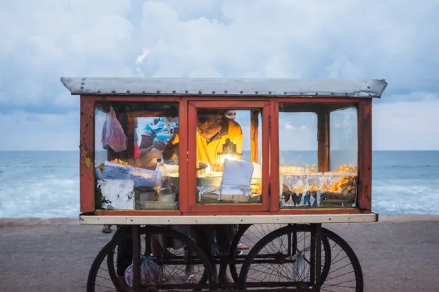 A man sells homemade snacks from his cart on the promenade by the Galle Face Hotel, Colombo, Sri Lanka. Shortly after this image was taken there was a huge downpour and everyone had to run for shelter”. (Photo by John Marsland/The Guardian)