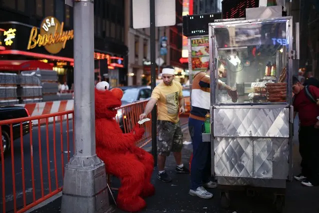 Jorge, an immigrant from Mexico, dressed as the Sesame Street character Elmo, exchanges his tips for larger bills from a street food car vendor in Times Square, New York July 30, 2014. (Photo by Eduardo Munoz/Reuters)