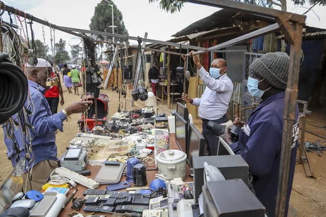 Onesmus Mauta, center, and Masumba, right, wear masks as they speak to a client, left, at their secondhand electronics street stall in the Kibera neighbourhood of Nairobi, Kenya Friday, March 20, 2020. (Photo by Patrick Ngugi/AP Photo)