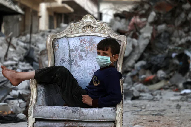 A child sits on a couch found in a street, ravaged by pro-regime forces air strikes, in the town of Ariha in the southern countryside of the Idlib province on April 11, 2020. Several weeks into a fragile truce that took effect as the novel coronavirus outbreak was turning into a pandemic, hundreds among nearly one million who fled their homes during a deadly regime offensive against the jihadist-dominated region of Idlib  have returned to Ariha, thinking that it is  better than risking their children catch the Covid-19 in  packed displacement camps. (Photo by Aaref Watad/AFP Photo)