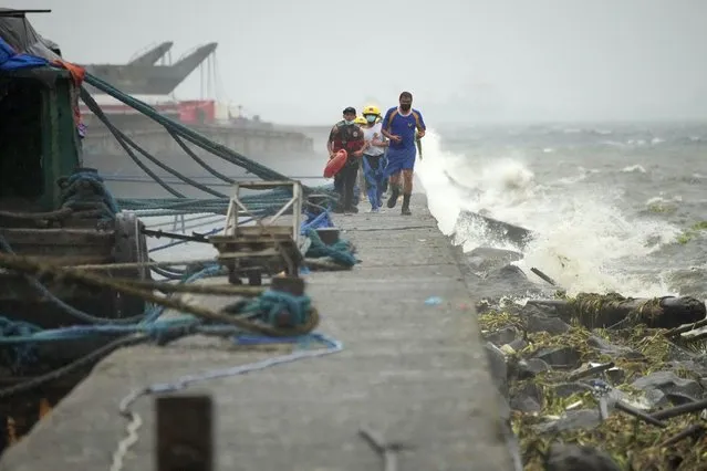 Rescuers run as they check residents living at the seaside slum district of Tondo while Typhoon Noru approaches Manila, Philippines, Sunday, September 25, 2022. The powerful typhoon shifted and abruptly gained strength in an “explosive intensification” Sunday as it blew closer to the northeastern Philippines, prompting evacuations from high-risk villages and even the capital, which could be sideswiped by the storm, officials said. (Photo by Aaron Favila/AP Photo)