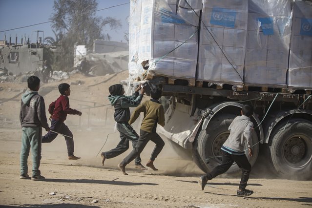 Palestinians chase humanitarian aid trucks that arrived through the Kerem Shalom crossing from Egypt into the Gaza Strip, in Rafah, Tuesday, January 21, 2025. (Photo by Jehad Alshrafi/AP Photo)