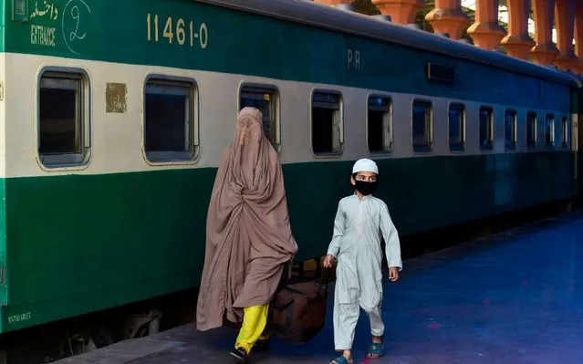 A woman and a child carry their bag as they arrive to board a train to Rawalpindi at a station after the government eased a lockdown imposed to prevent the spread of the COVID-19 coronavirus in Lahore on May 20, 2020. (Photo by Arif Ali/AFP Photo)