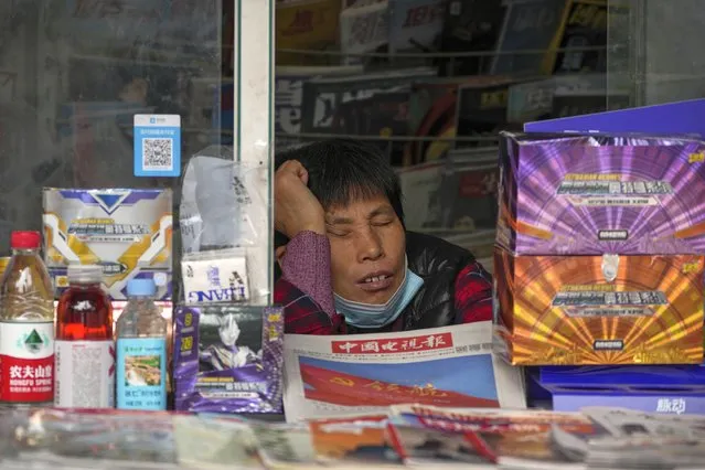 A vendor wearing a face mask takes a nap inside a newsstand selling newspapers in Beijing, Thursday, October 13, 2022. (Photo by Andy Wong/AP Photo)