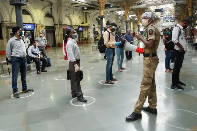 A railway police official makes an announcement on a loudspeaker telling commuters to stand inside the designated circles to maintain social distancing as they wait to board a train at a railway station after some restrictions were lifted during a lockdown to slow the spread of the coronavirus disease (COVID-19) in Mumbai, India, June 22, 2020. (Photo by Francis Mascarenhas/Reuters)