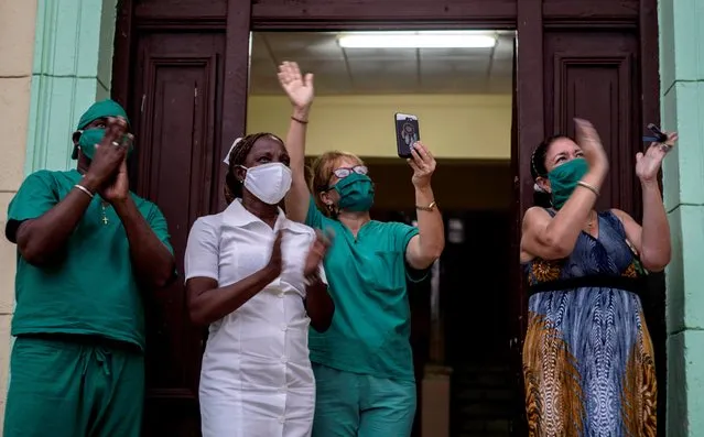 Medical staff applaud while looking out onto a balcony where opera singer Andres Sanchez Joglar serenades his neighborhood in Havana, Cuba, Sunday, May 31, 2020. Andres sings every Sunday in the afternoon from his balcony in a central building in Havana to encourage neighbors in social isolation due to the coronavirus. (Photo by Ramon Espinosa/AP Photo)