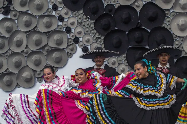 Mexican regional dancers perform in front of a mosaic made with Mexican traditional hats, during a Guinness record ceremony to the world's largest mosaic made with hats, in Guadalajara, Mexico, on August 26, 2016. The mosaic was made with more than a thousand hats and measures ten meters high. (Photo by Hector Guerrero/AFP Photo)