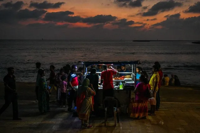 In this picture taken on October 29, 2022, visitors buy street food from a vendor selling prawns and crabs from a cart at the Galle Face promenade in Colombo. (Photo by Ishara S. Kodikara/AFP Photo)
