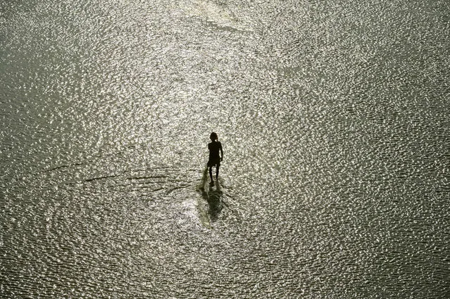 A man with a nets to catch fish walks in a shallow section of the Ganges River in Prayagraj on November 18, 2022. (Photo by Sanjay Kanojia/AFP Photo)