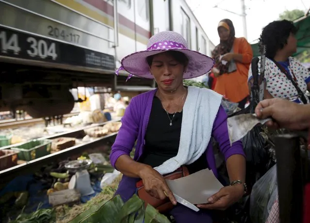 A vendor (C) serves a customer at a vegetable market as a commuter train passes in Jakarta, October 2, 2015. (Photo by Reuters/Beawiharta)