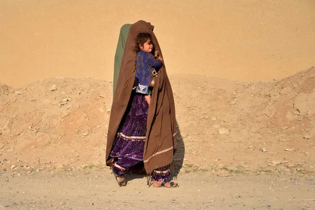 A woman carrying a child walks along a roadside in Zhari district of Kandahar province on February 15, 2023. (Photo by Sanaullah Seiam/AFP Photo)