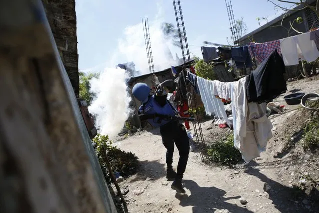 A U.N. soldier from Senegal hurls a tear gas grenade as troops clash with rock-throwing neighborhood residents outside a U.N. base in Les Cayes, Haiti, Saturday, October 15, 2016. Residents said clashes with the peacekeepers began when trucks carrying food aid arrived at the base. (Photo by Rebecca Blackwell/AP Photo)