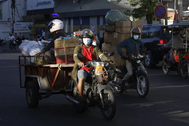 Motorcycle delivery riders wear face masks to curb the spread of the coronavirus transport goods in Phnom Penh, Cambodia, Tuesday, December 8, 2020. Although Cambodia has reported only 350 cases of the virus since the pandemic began, most of them acquired abroad with no confirmed deaths, a rare local outbreak in late November has prompted authorities to close state schools until the start of the next school year, and ordered the closure of all theaters, museums and prohibition of public concerts for two weeks. (Photo by Heng Sinith/AP Photo)